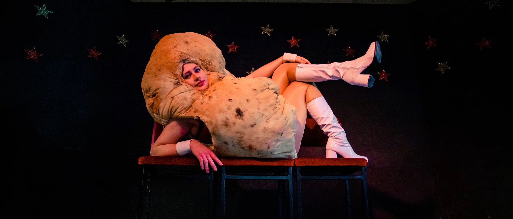 A woman dressed as a giany potato reclines glamourously on a couch
